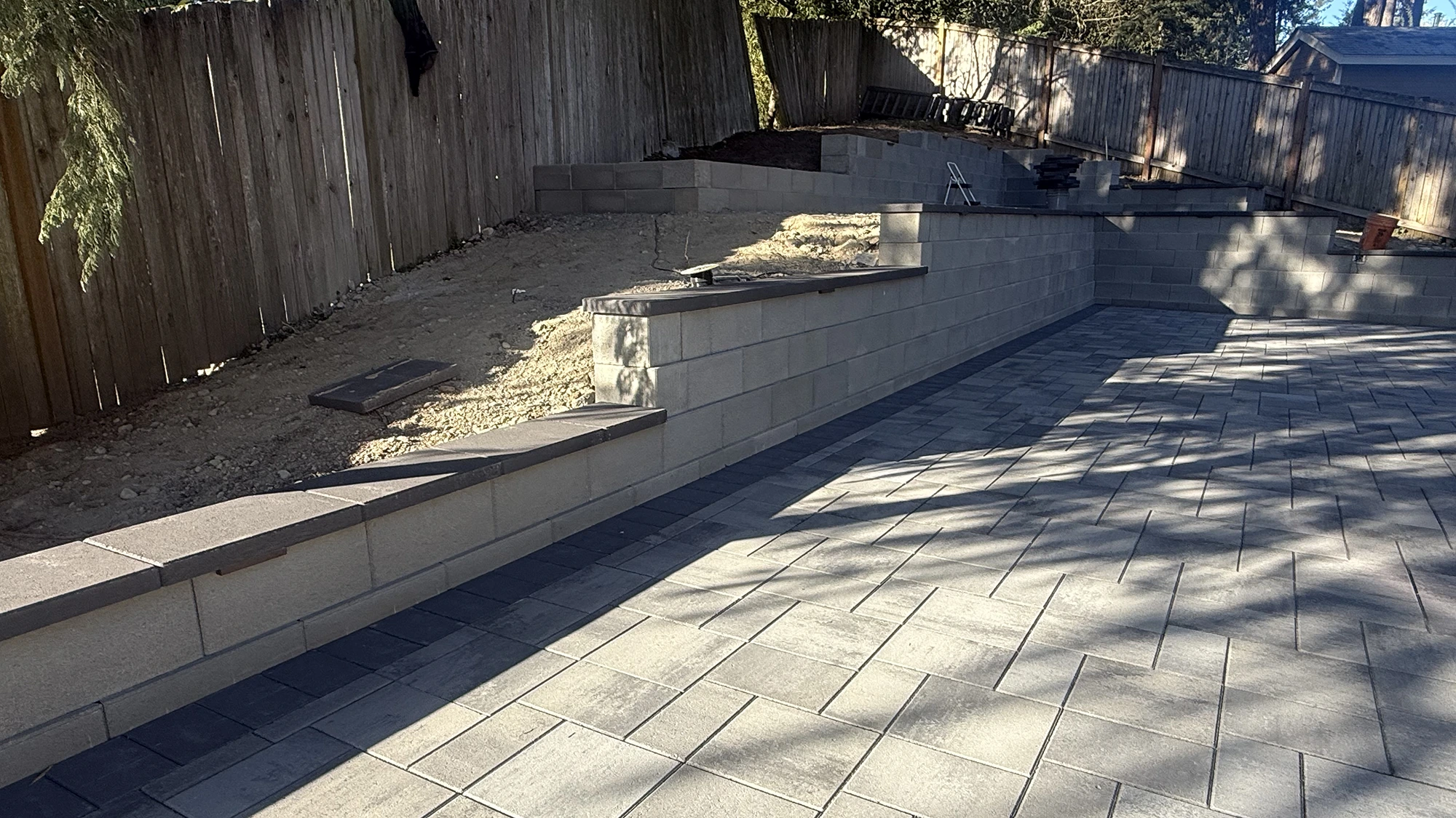 Tiered block retaining wall with dark caps above the new paver patio in Bothell
