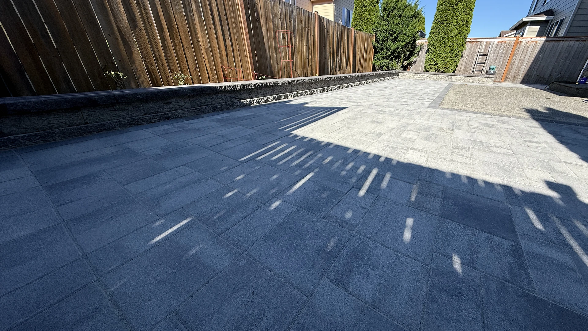 Large backyard paver patio in afternoon sun with block retaining wall in Mill Creek, WA