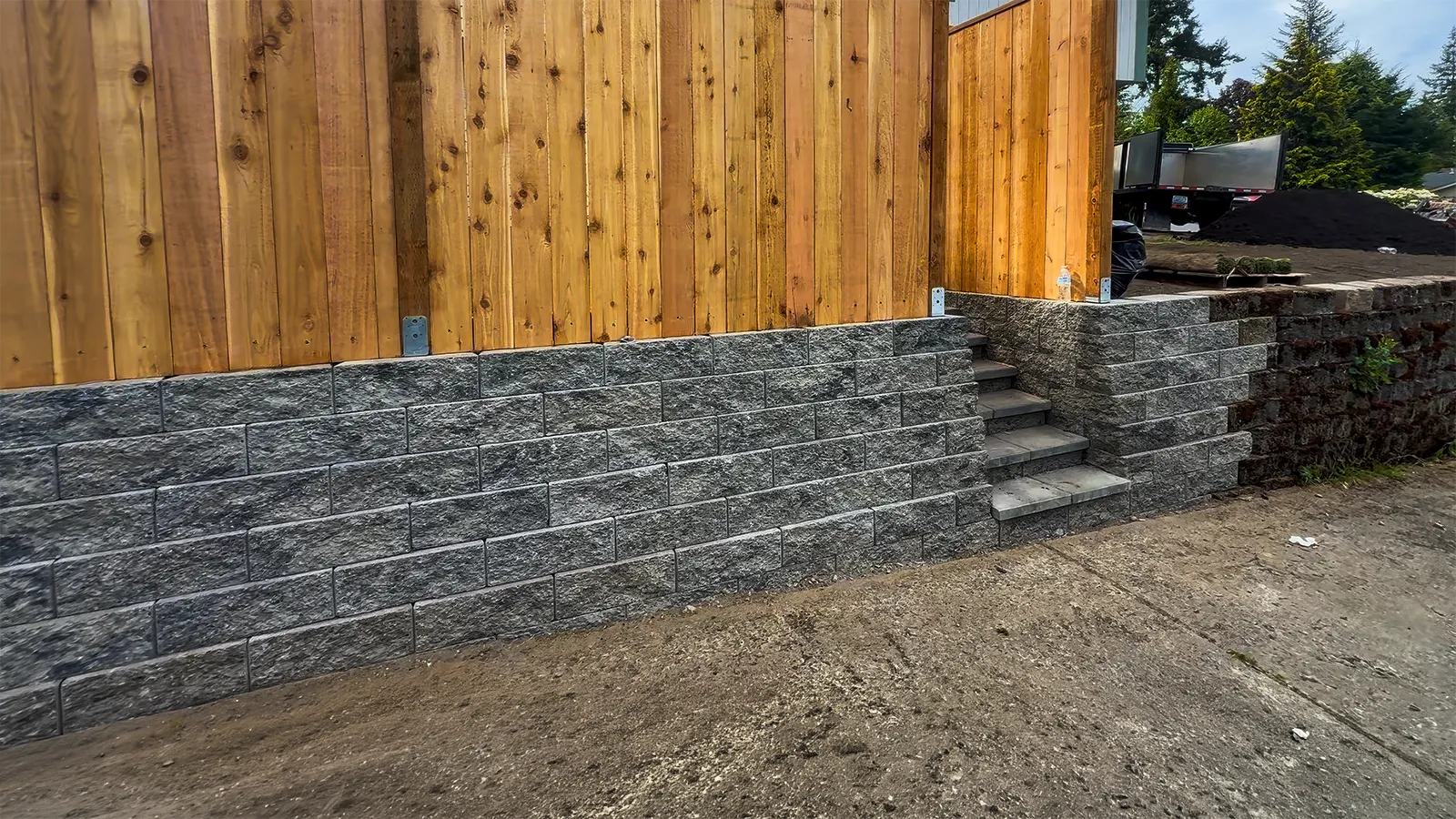 Completed curved concrete block retaining wall with a wood fence on top in Federal Way, WA