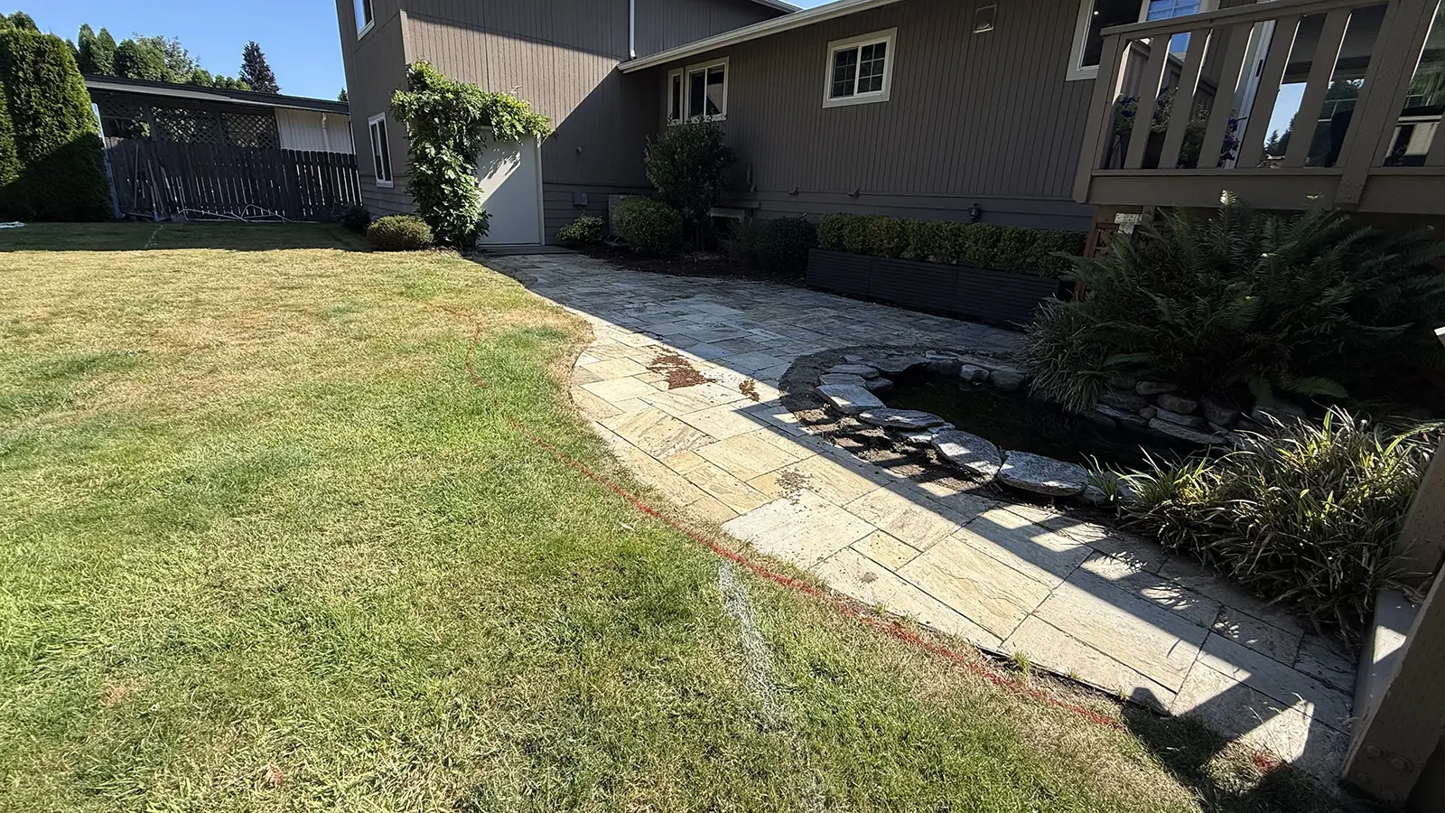 Worn flagstone path and lawn beside a pond before paver installation in Bothell, WA