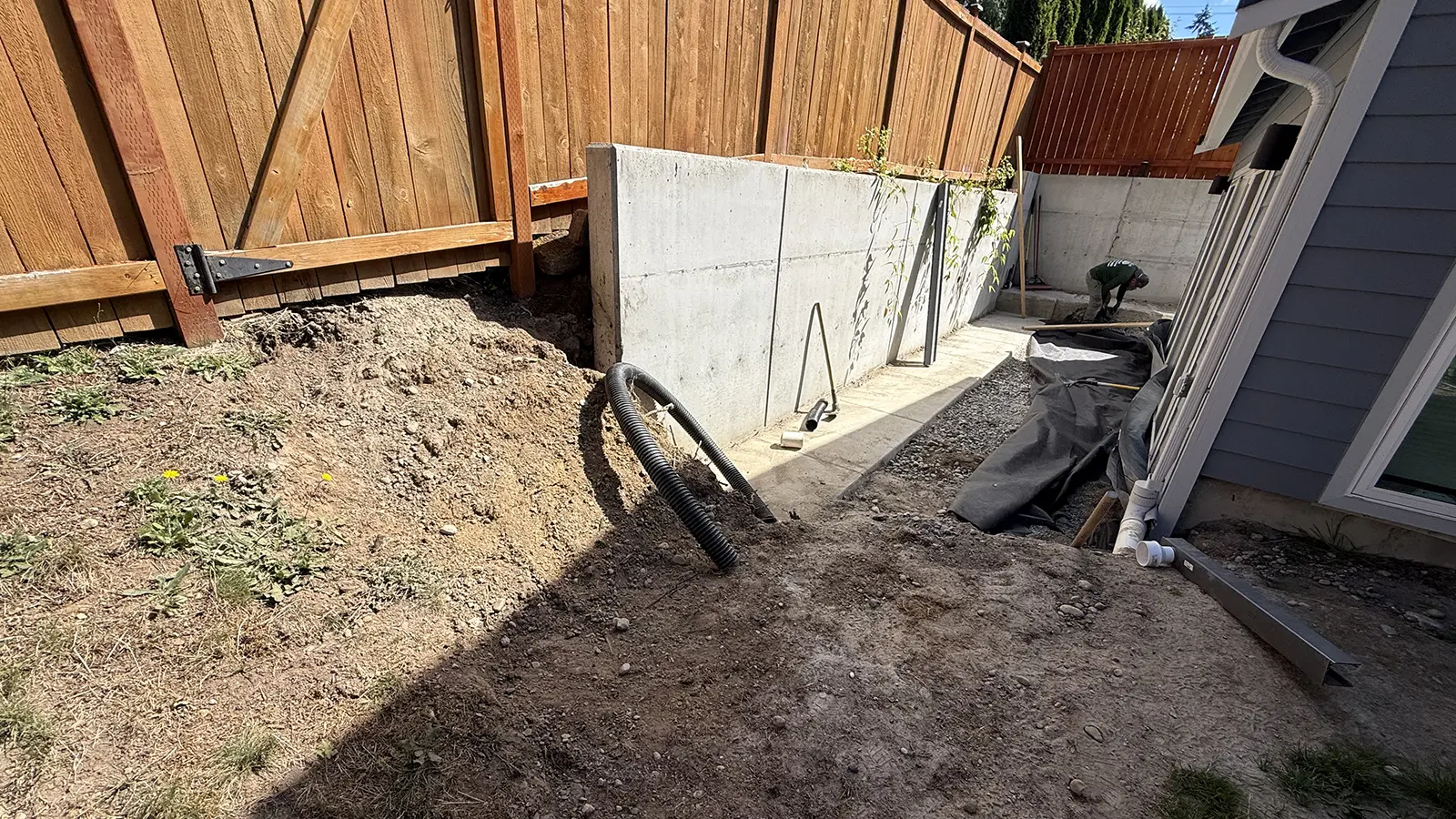 Bare dirt slope and drain pipe beside the retaining wall before paver walkway installation in Bothell, WA