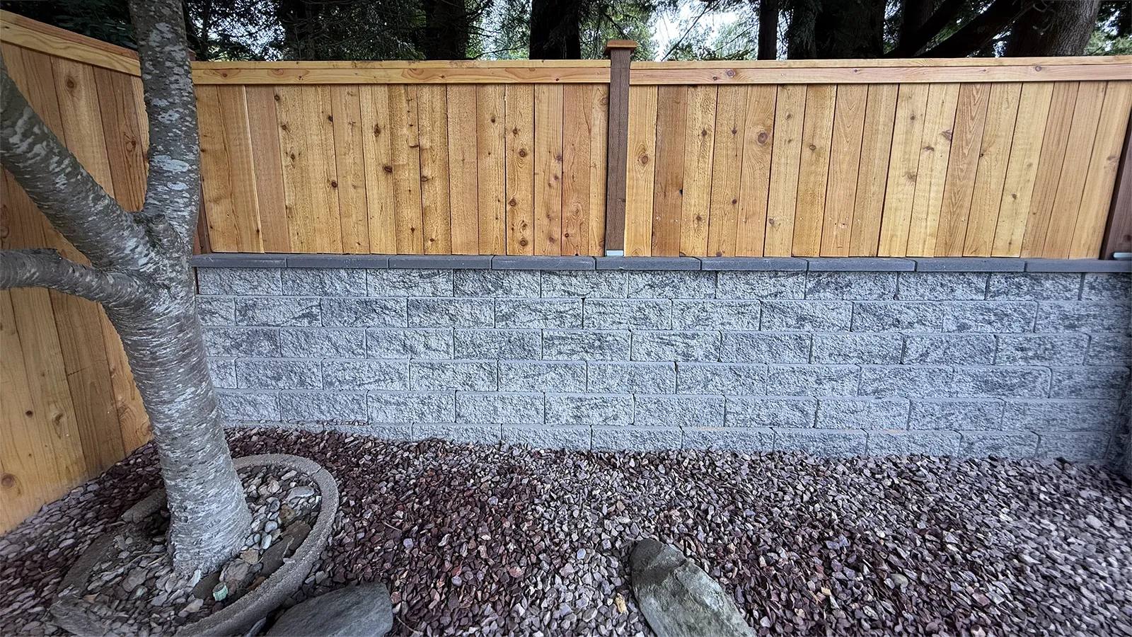 Cedar fence mounted on a concrete block retaining wall with gravel bed in Seattle, WA