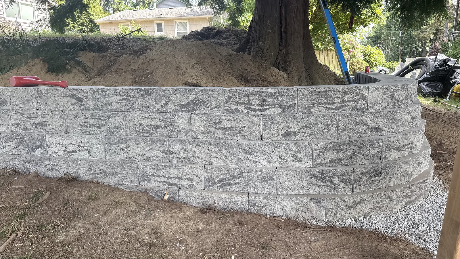 Split-face concrete block retaining wall curving around a cedar tree in Seattle, WA