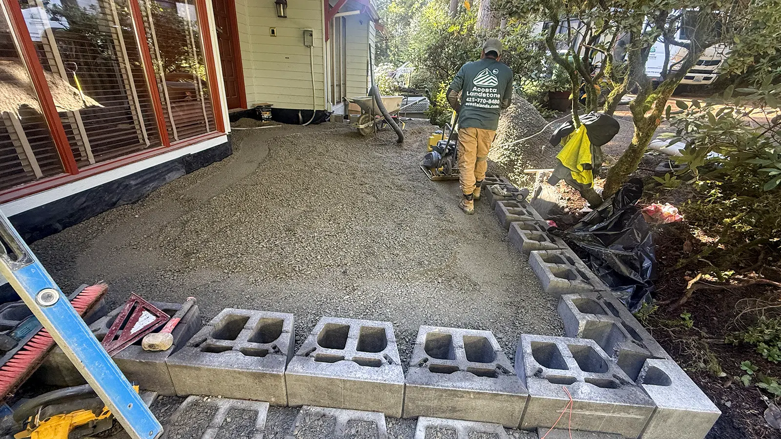 Compacting the gravel base inside the block walls of a raised paver patio in Bothell, WA