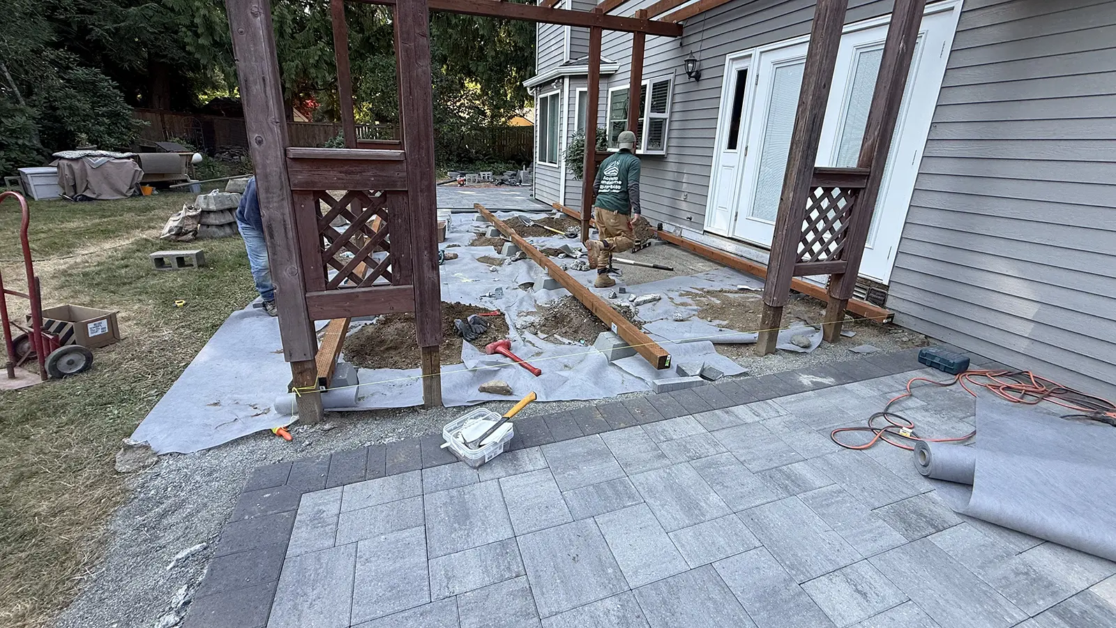 Paver patio installation with charcoal border and deck beams set on footings in Duvall, WA