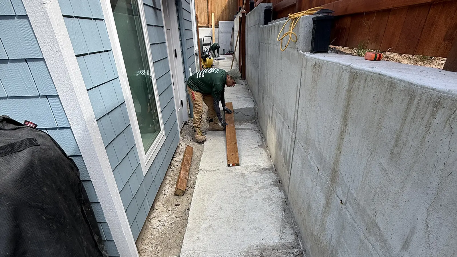Crew preparing a narrow side yard along a concrete retaining wall for a paver walkway in Bothell, WA