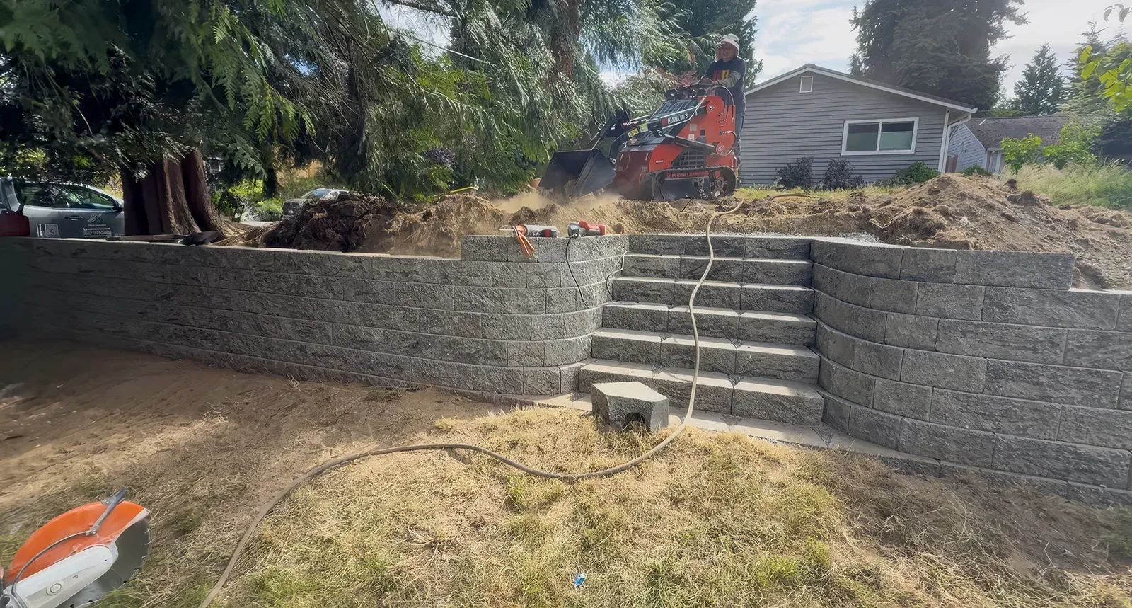 Mini loader backfilling behind a retaining wall with built-in block steps in Seattle